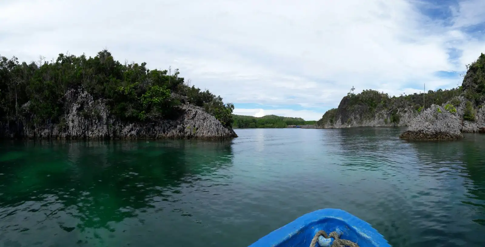 View forward from a small boat crossing calm water between limestone cliffs